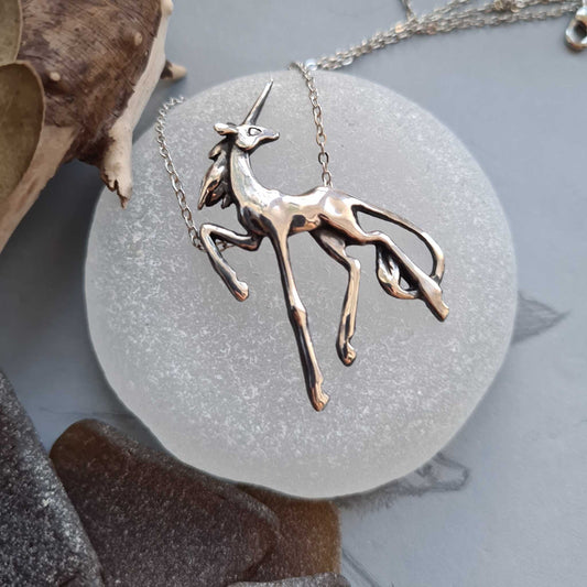 Silver Unicorn necklace lying on a rounded sea glass disc, showcasing its fairytale-like movement and form.