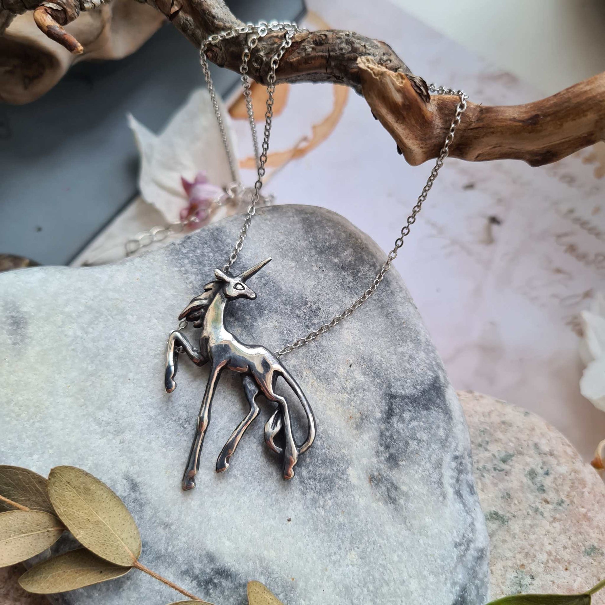 Silver Unicorn necklace photographed on gray marble, showing its slender, whimsical design.