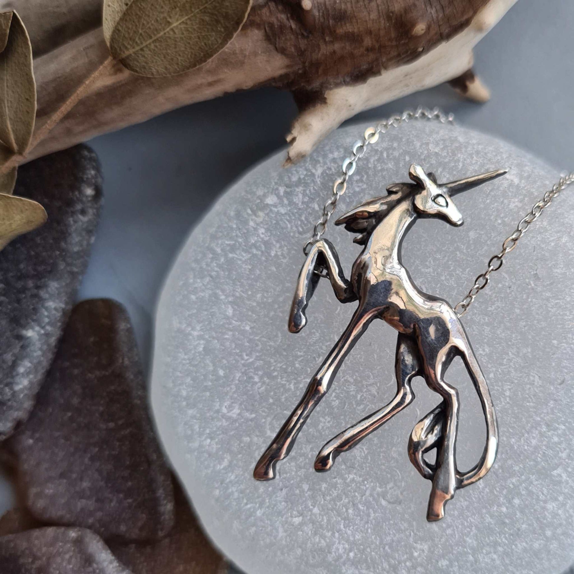 Close-up of a silver Unicorn necklace resting on white sea glass, highlighting the graceful limbs, lifted hoof and polished finish.