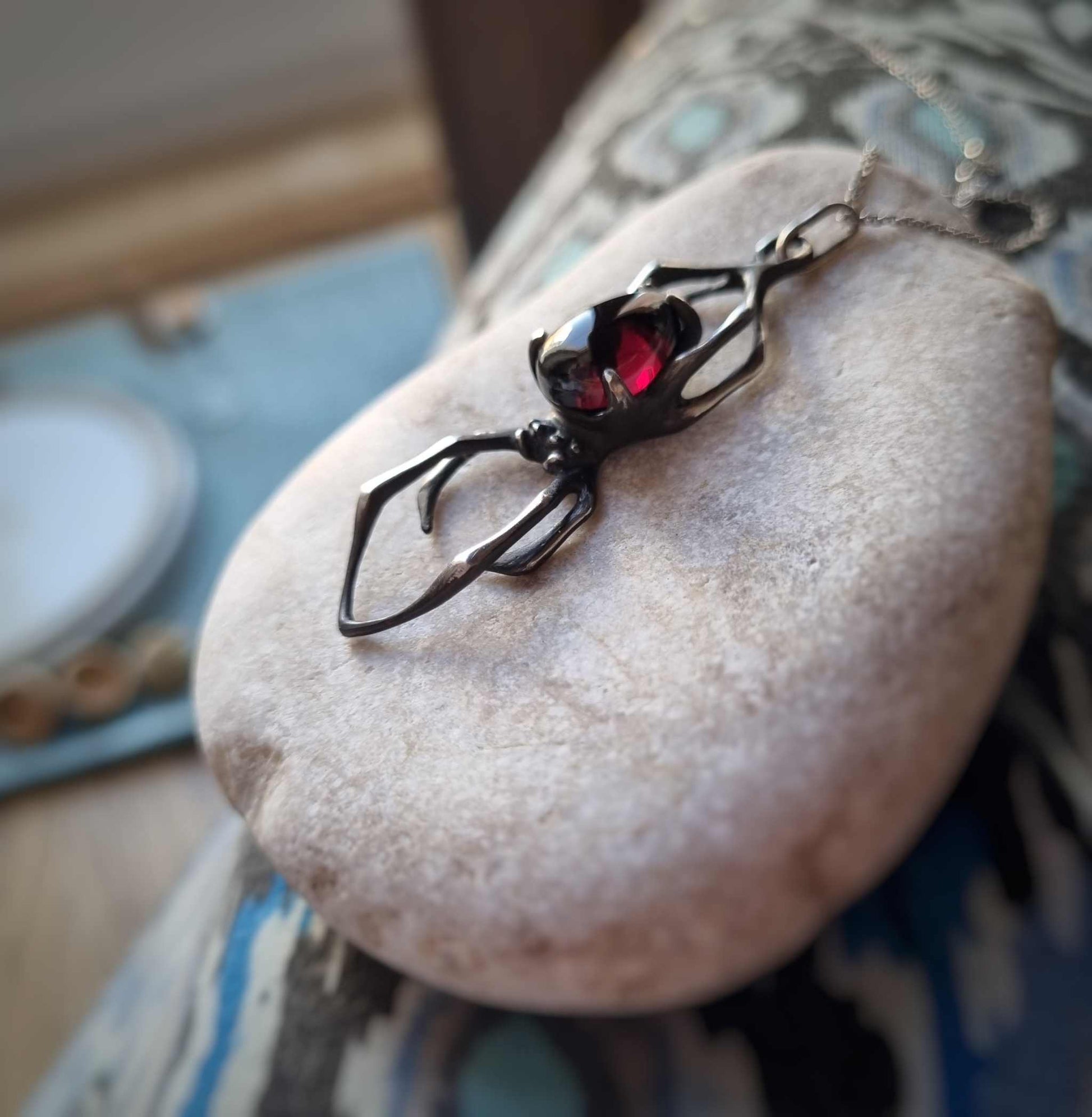 Sculptural Silver spider necklace styled on a white pebble
