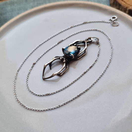Close-up of handmade silver Spider necklace featuring London blue topaz, displayed on a plate with coiled chain