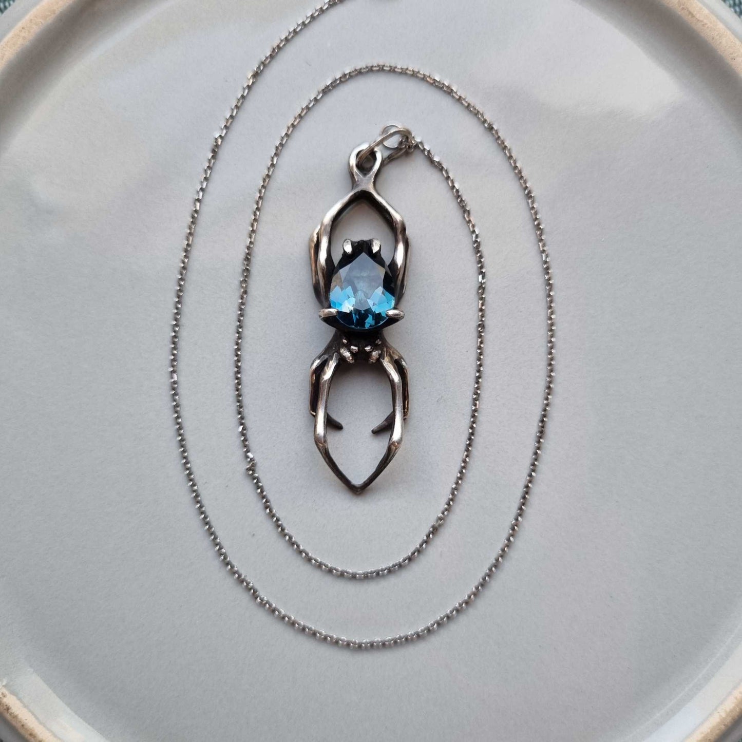Top view of oxidized silver Spider pendant with deep blue topaz and delicate chain arranged in circles