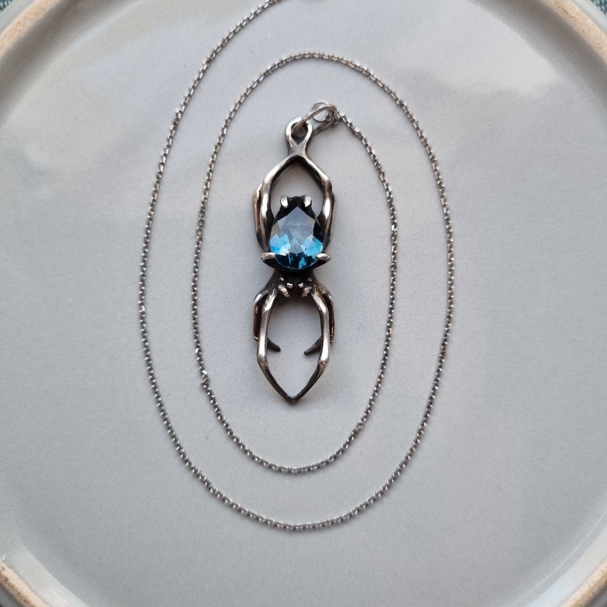 Top view of oxidized silver Spider pendant with deep blue topaz and delicate chain arranged in circles