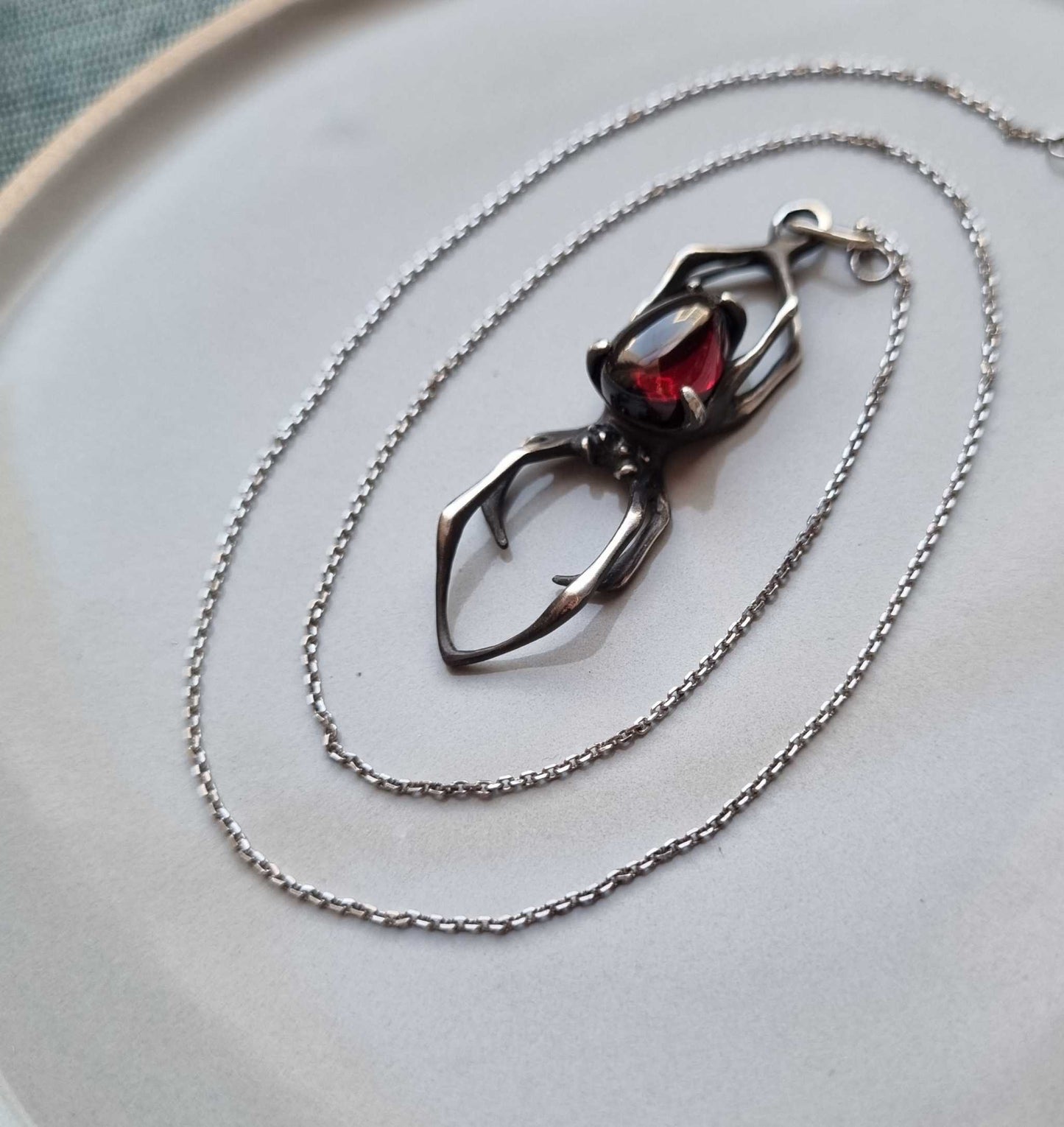 Garnet spider pendant in sterling silver photographed from above – oxidized finish detail and spiral chain