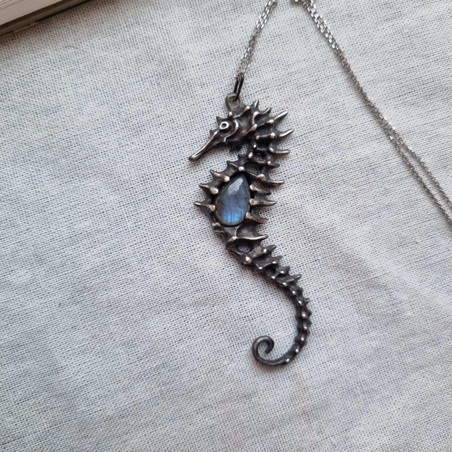 Silver Seahorse necklace featuring a striped labradorite, displayed on textured linen fabric.