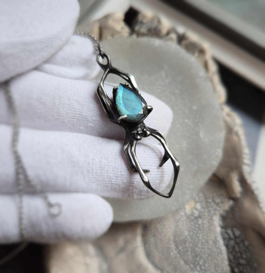 Silver Spider necklace with blue labradorite — close-up in gloved hand, showing gemstone glow and oxidized silver texture