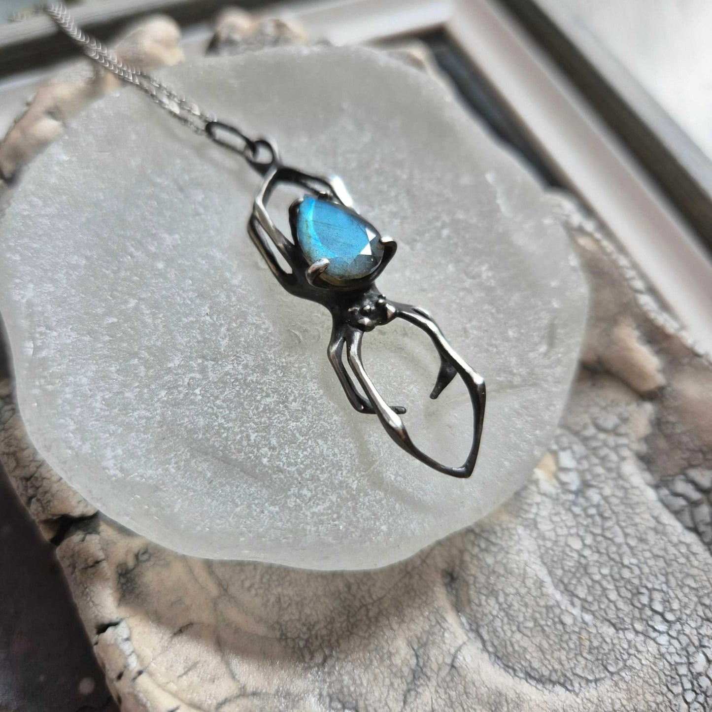 silver Spider necklace with faceted blue labradorite, resting on frosted ceramic dish