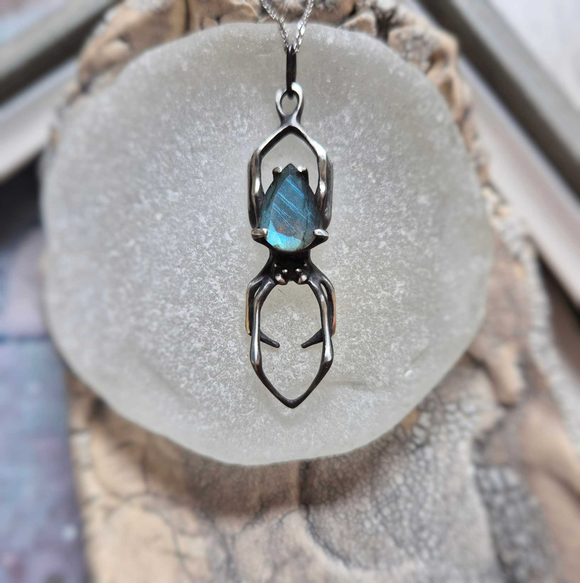 Handmade silver Spider necklace with blue labradorite gemstone, front view on display stone