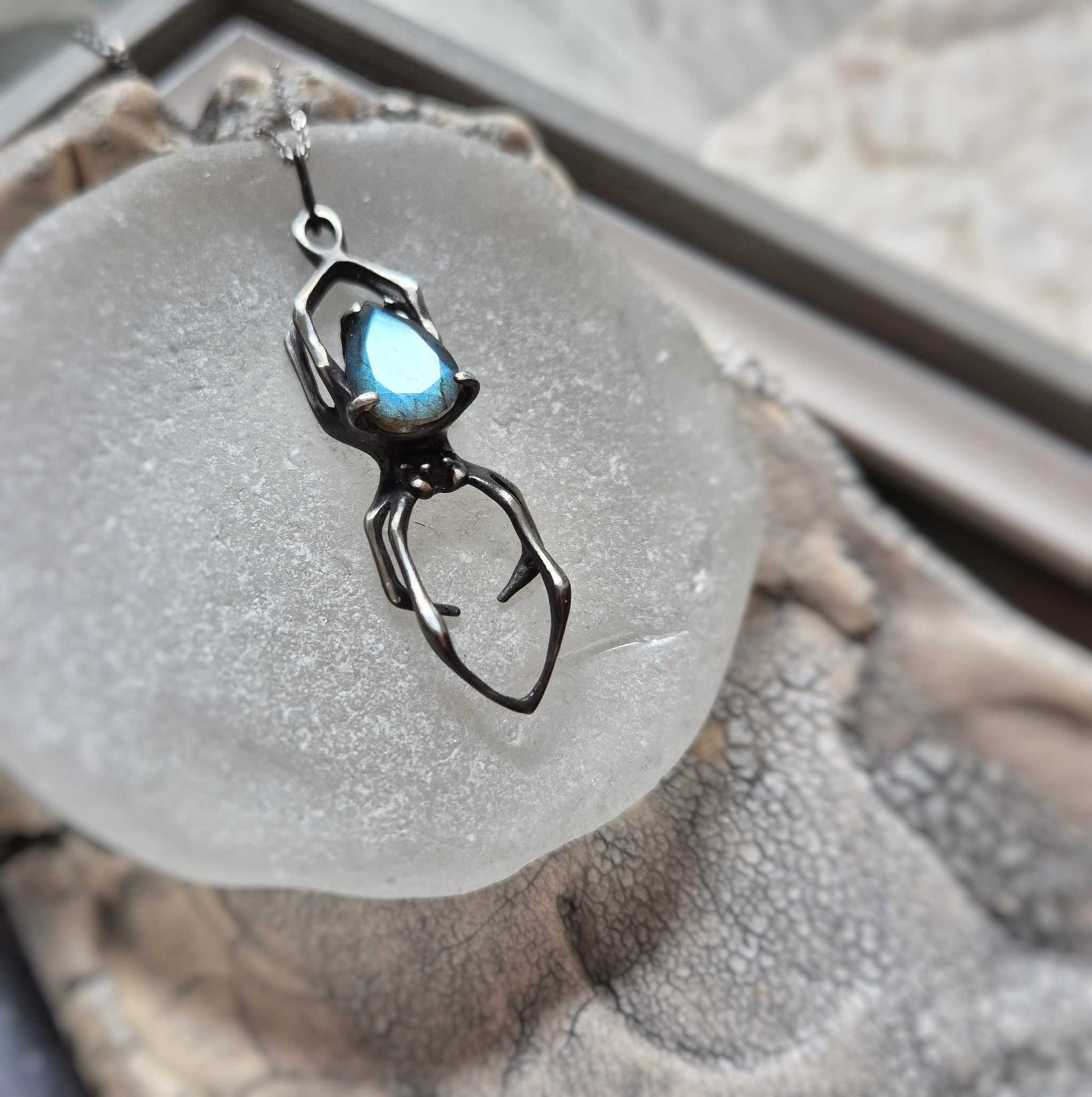 Blue labradorite Spider necklace in oxidized silver, shown on round ceramic base under soft light