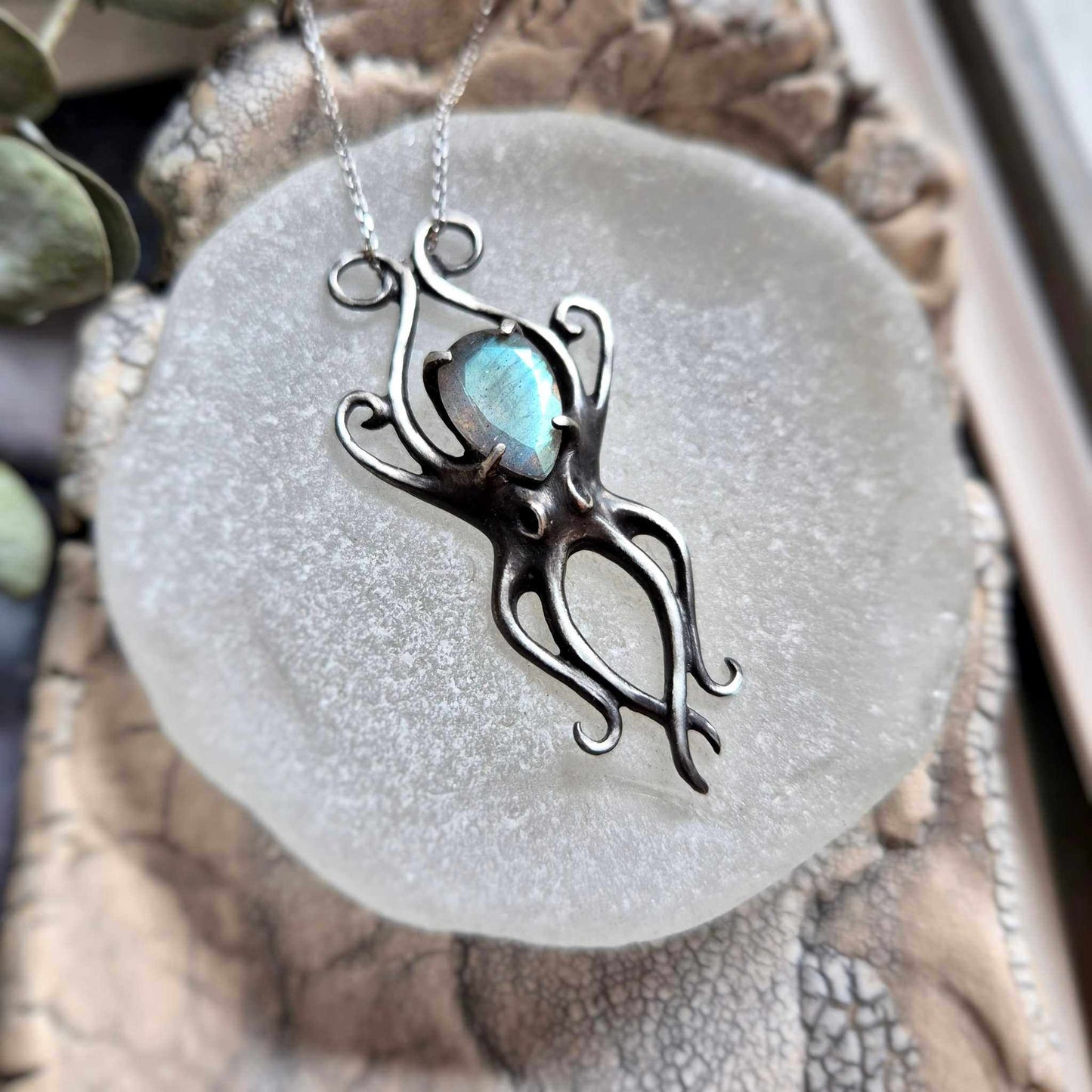 Silver Octopus necklace with cyan labradorite on a round stone plate, surrounded by seashells