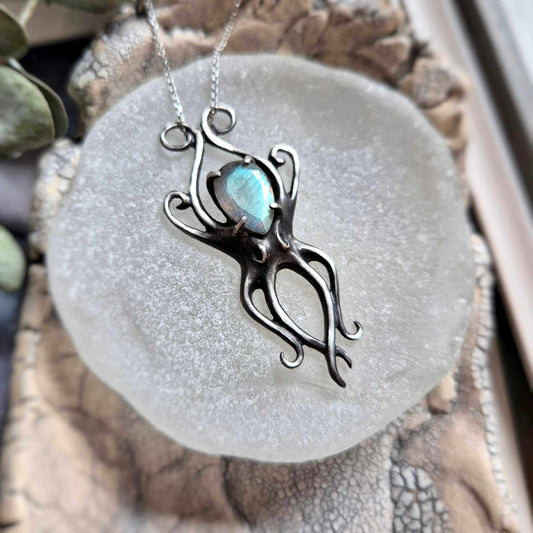 Silver Octopus necklace with cyan labradorite on a round stone plate, surrounded by seashells