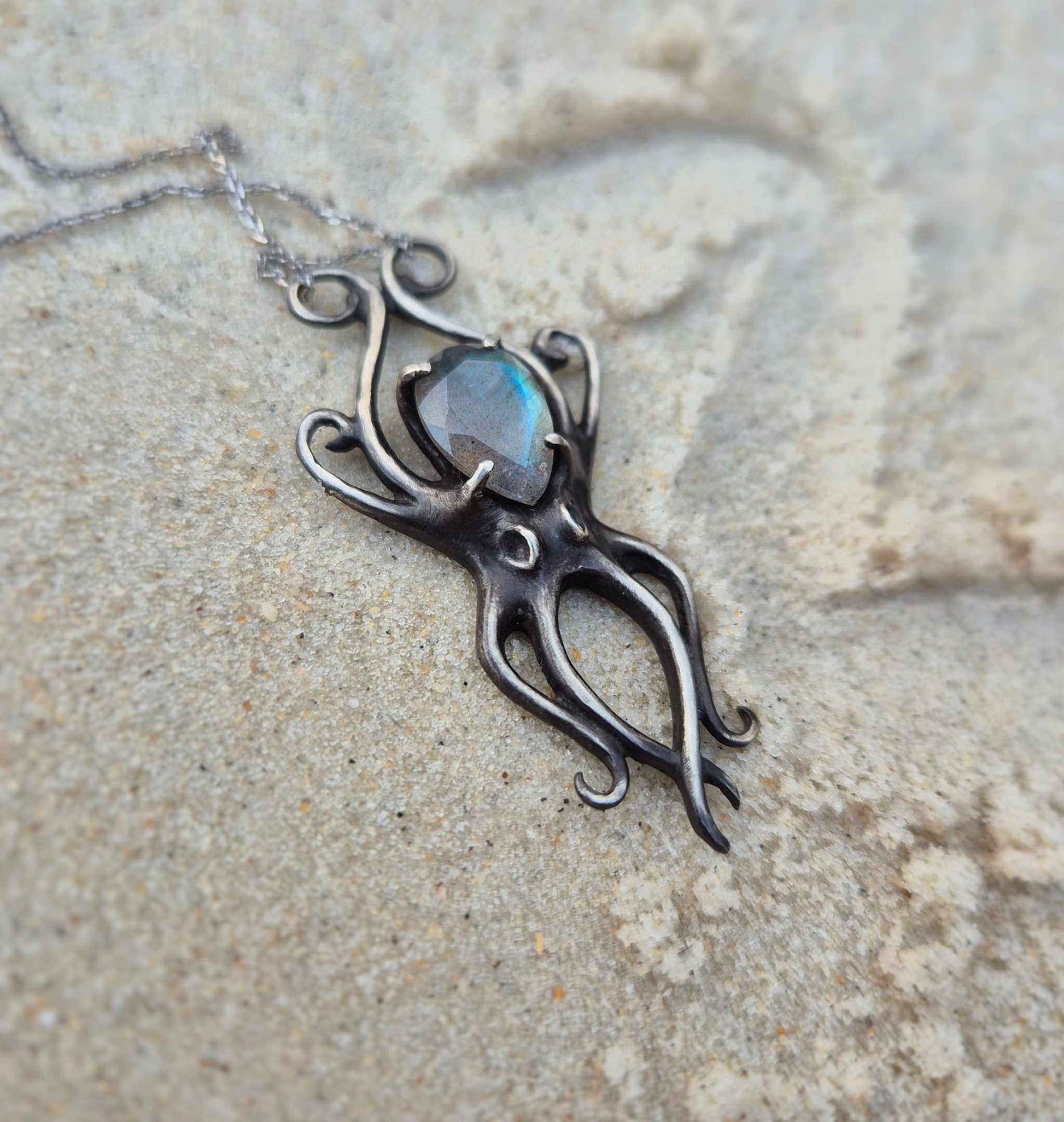 Silver Octopus necklace with bright labradorite placed on sandy background