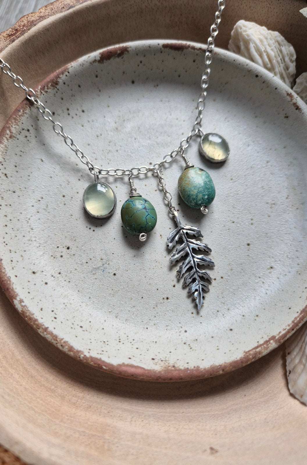 Detail of botanical silver turquoise  necklace with turquoise stones and soft green prehnite, arranged flat on a speckled clay dish.