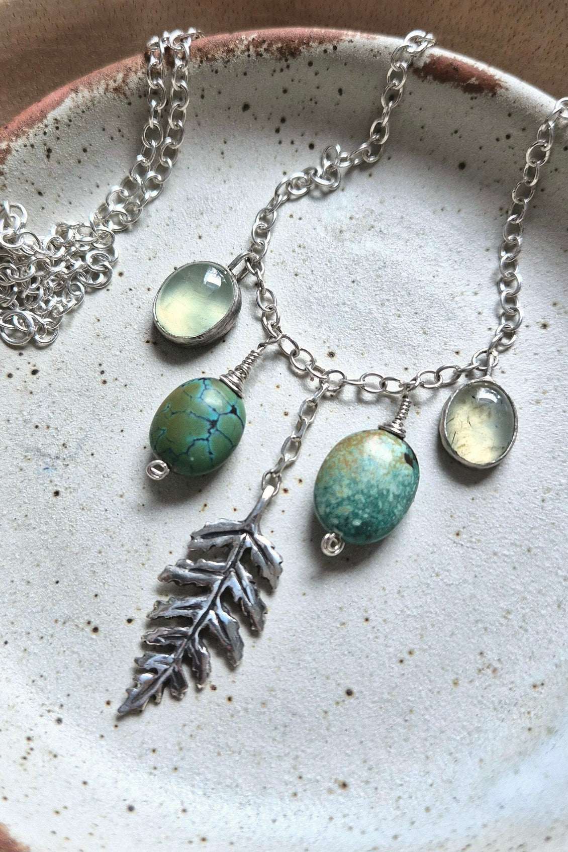 Nature-themed silver turquoise necklace with turquoise, prehnite, and a silver leaf charm, styled on a neutral ceramic dish for an earthy, organic look.