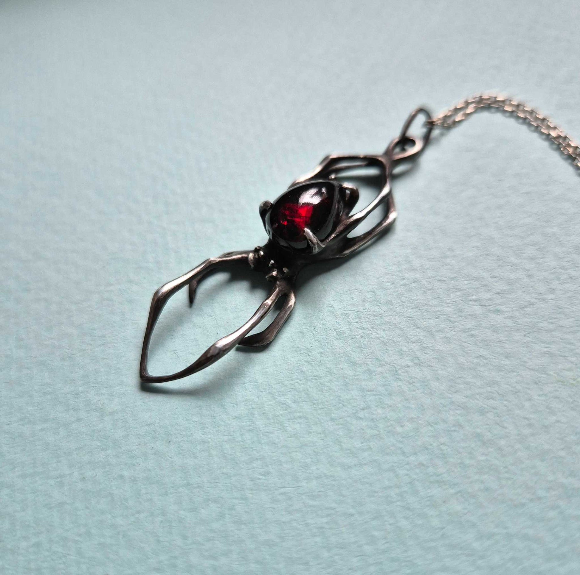 Side view of silver spider necklace with cherry-red garnet – handmade talisman pendant