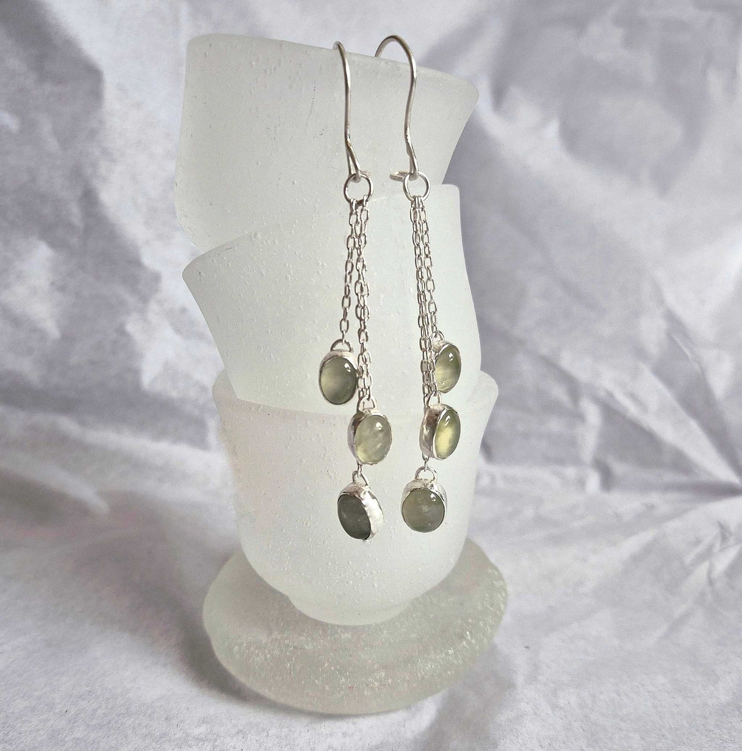 Green dangle earrings with natural prehnite cabochons on a white glass stand