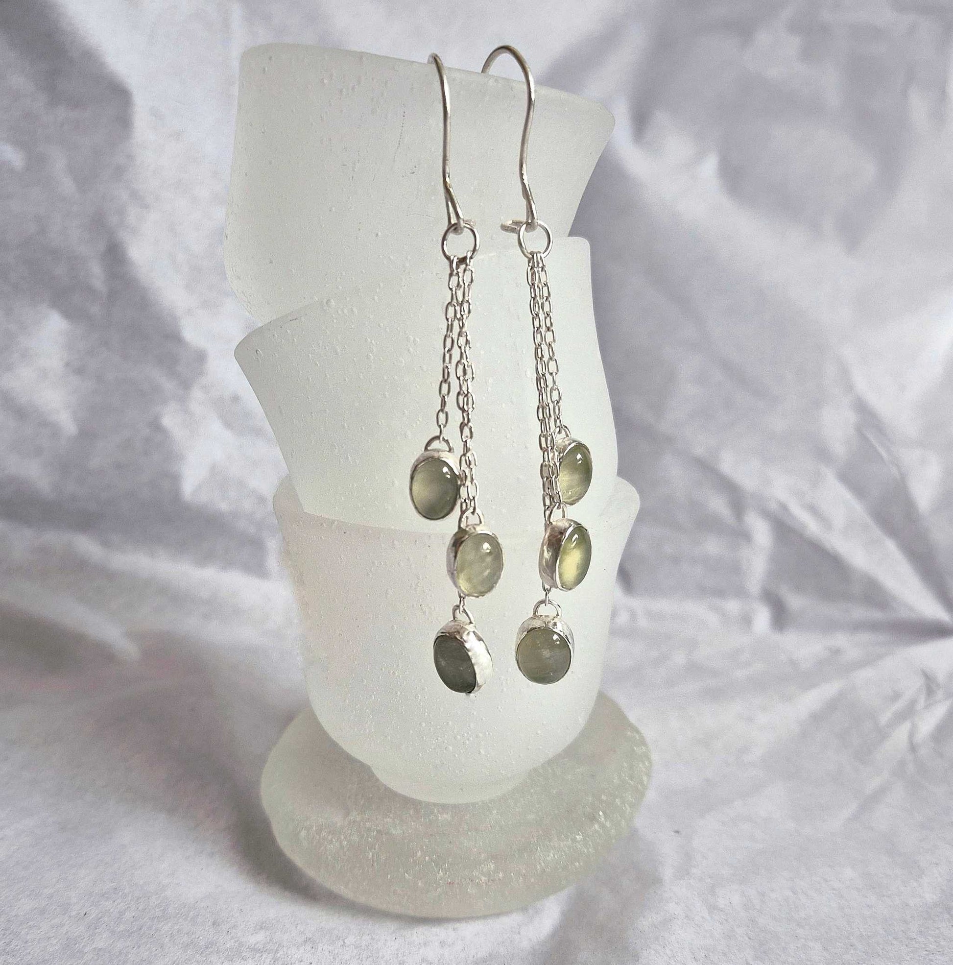 Green dangle earrings with natural prehnite cabochons on a white glass stand