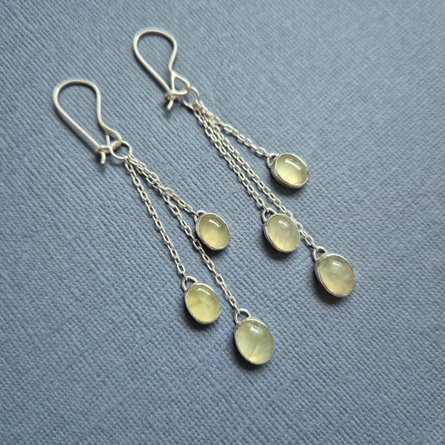 Handcrafted silver earrings with green prehnite drops on pastel blue background