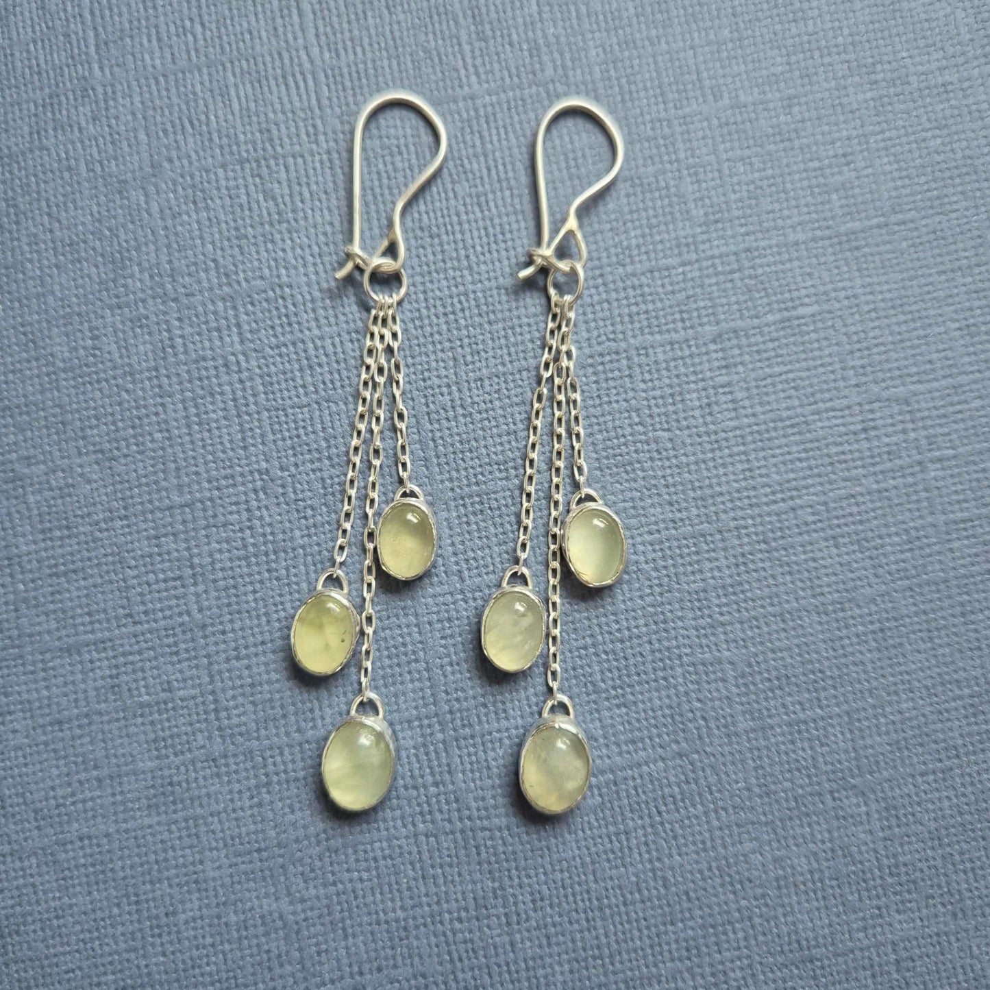 Silver green dangle earrings with two prehnite stones on soft blue background