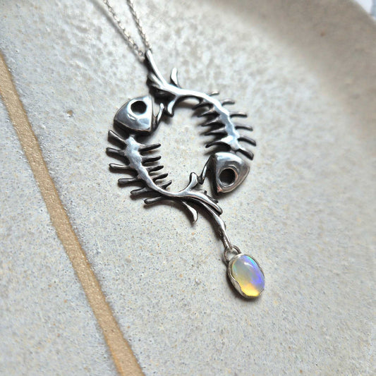 Artisan silver pendant with fishbone design and transparent opal. Circular skeletal fish form with dangling gemstone.
