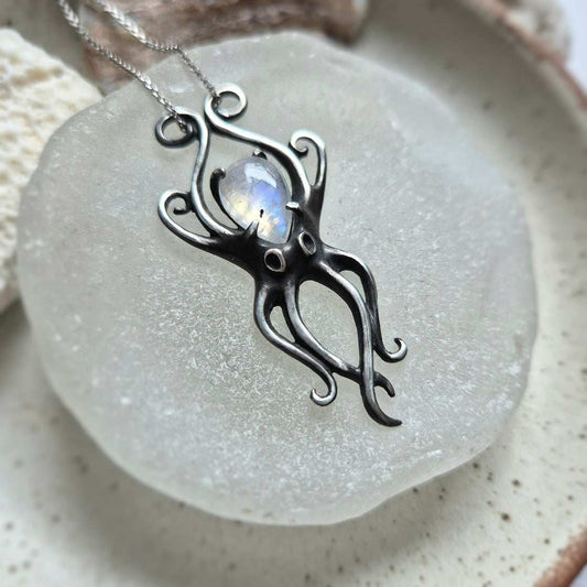 Silver Octopus necklace with rainbow moonstone, handmade and displayed on a glass plate.