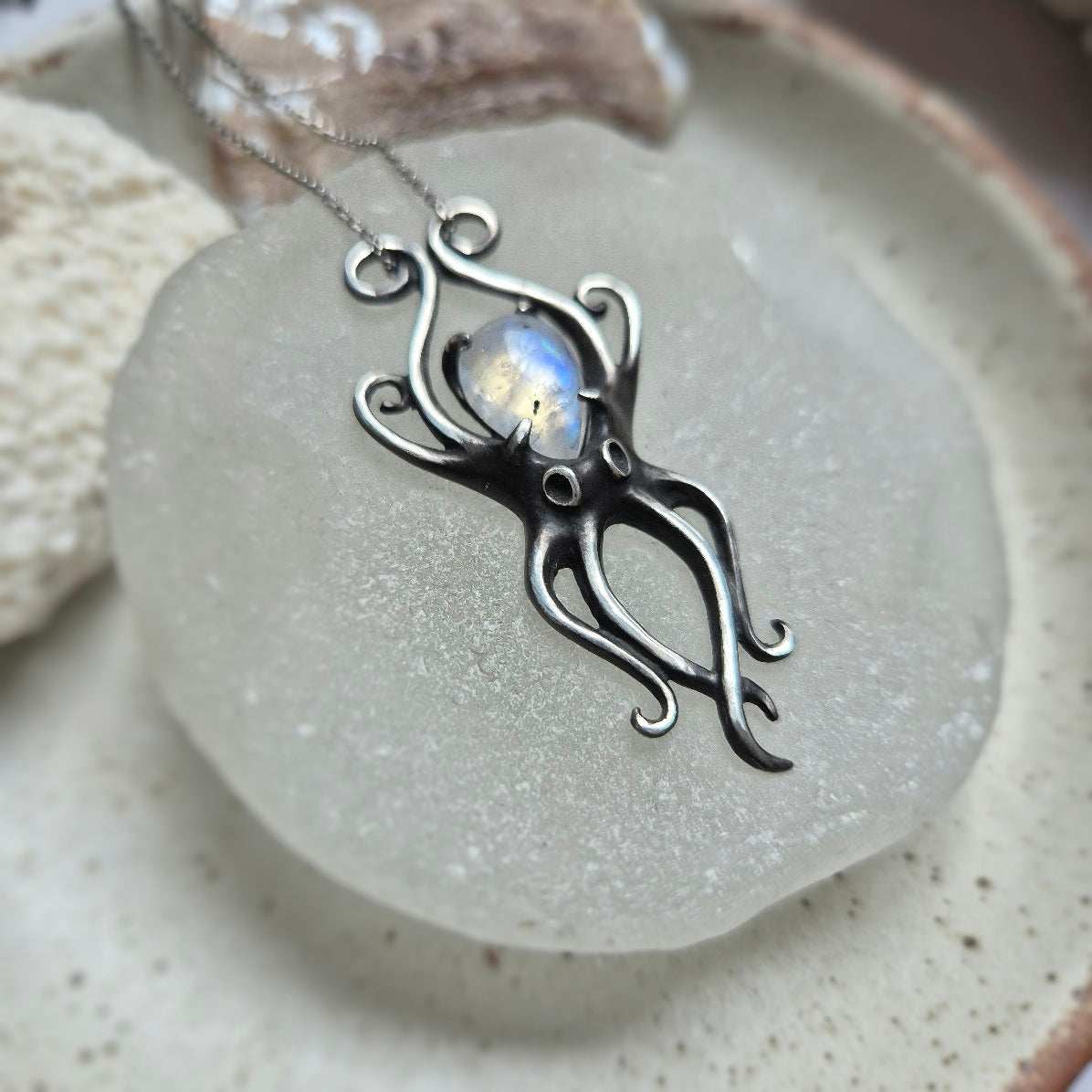Elegant silver Octopus necklace with natural rainbow moonstone cabochon, resting on a ceramic dish.