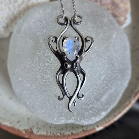 Handcrafted silver Octopus pendant featuring rainbow moonstone, photographed on neutral glass.