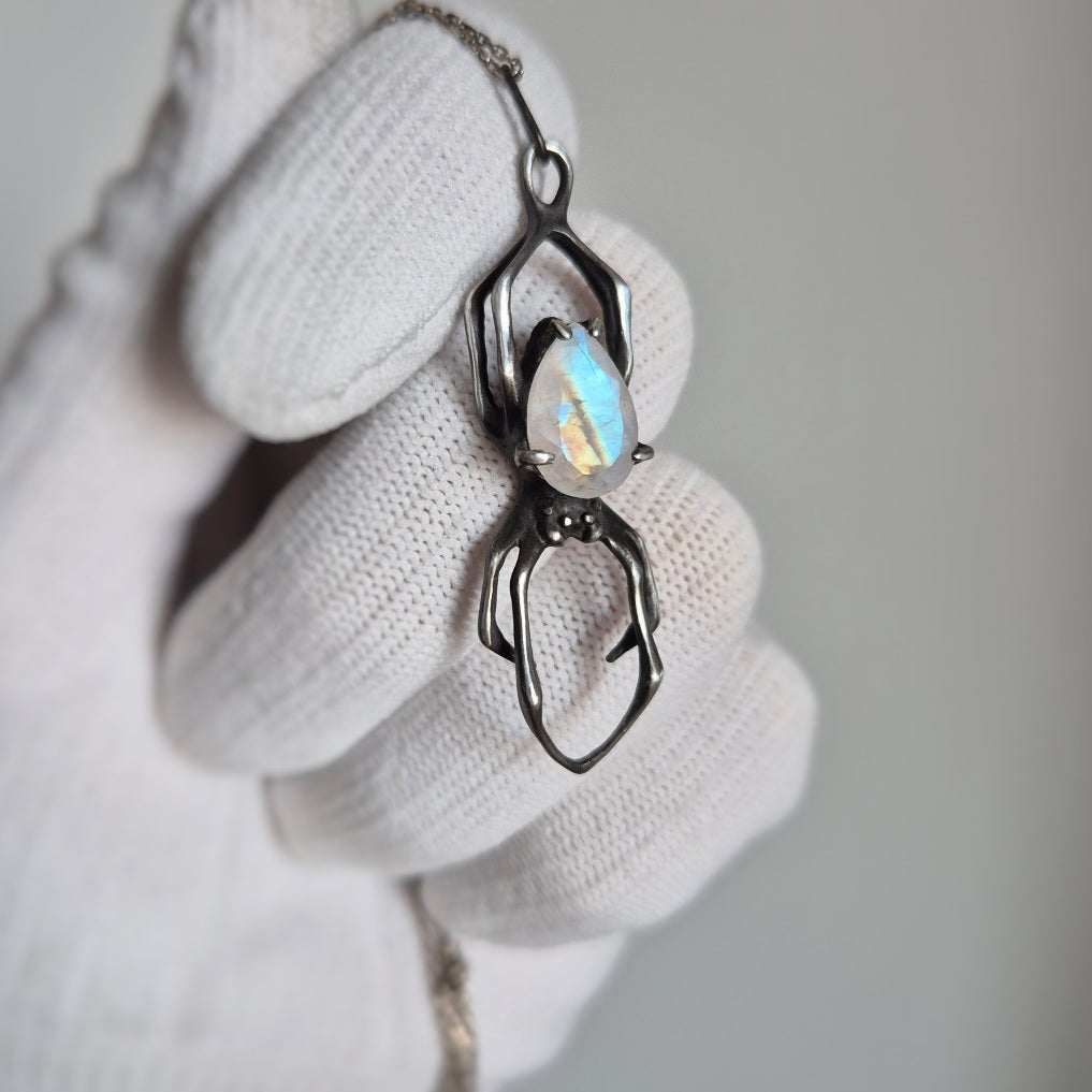 Oxidized silver Spider pendant with faceted rainbow moonstone held in gloved hand