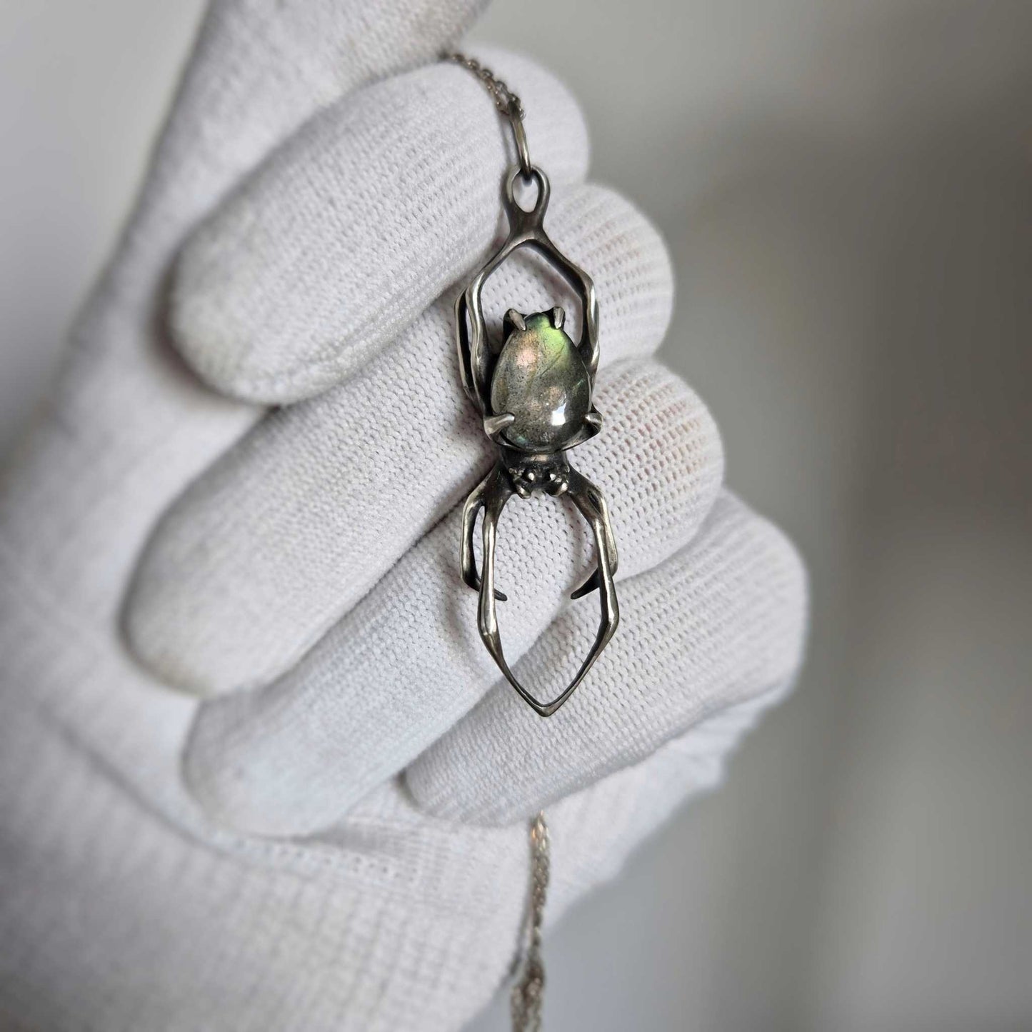 Close-up of silver Spider pendant with labradorite, held in a gloved hand