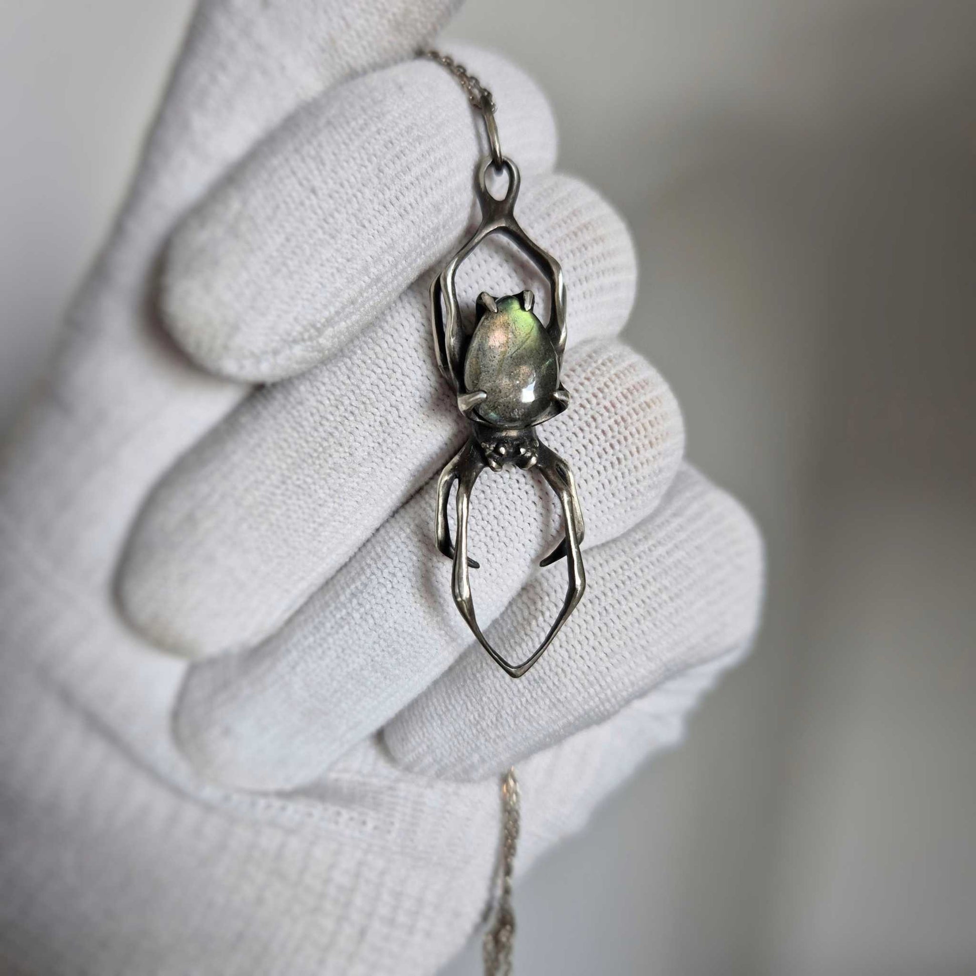 Close-up of silver Spider pendant with labradorite, held in a gloved hand