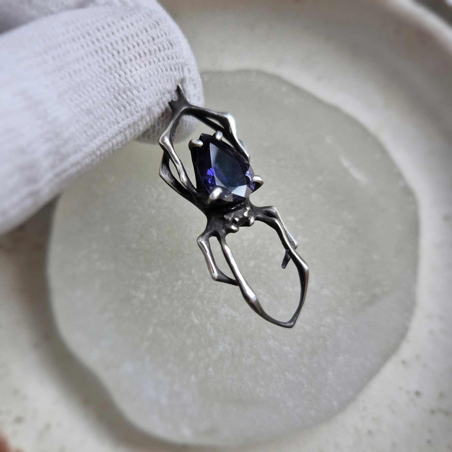 Close-up of silver Spider necklace with deep blue iolite sunstone gemstone, held against a neutral background