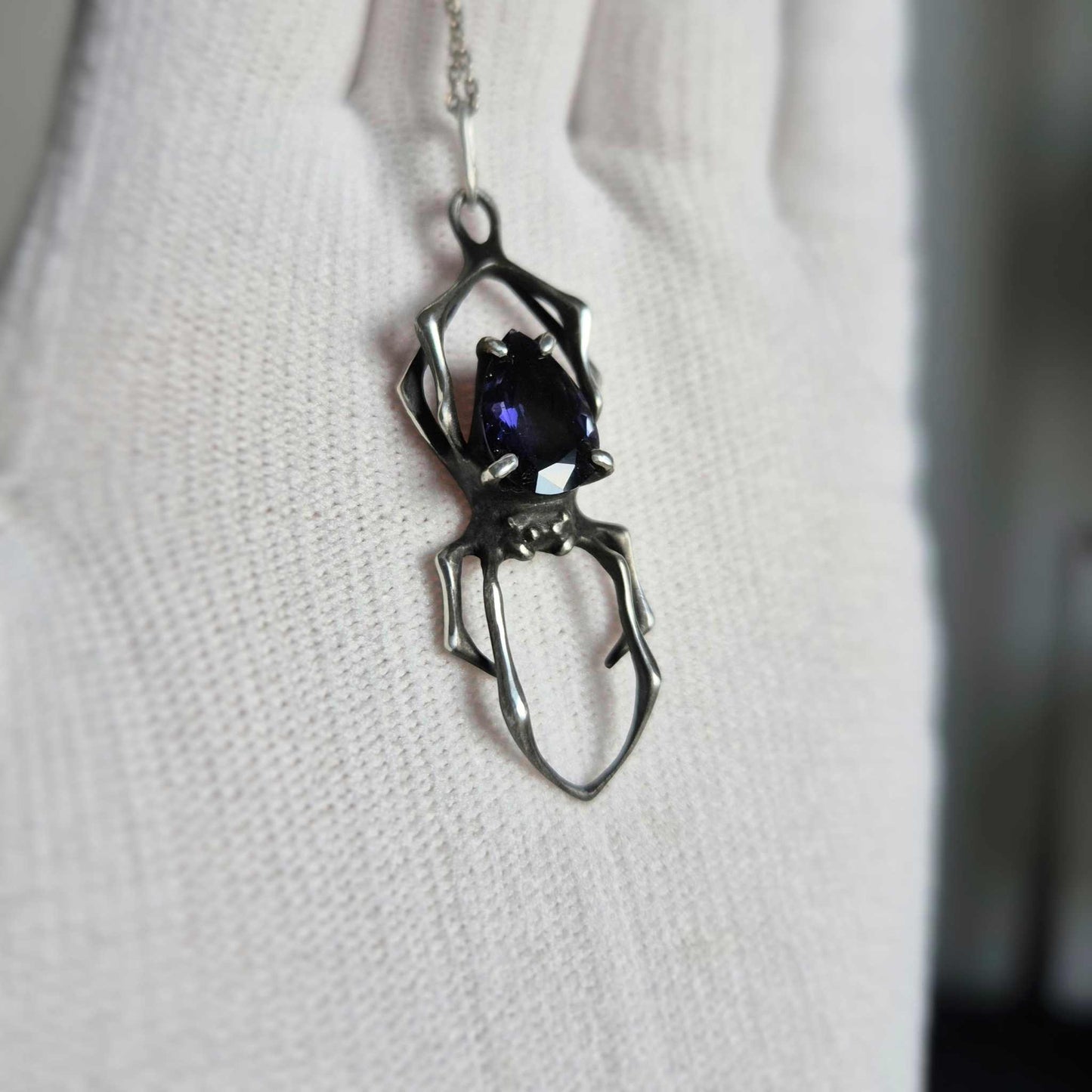 silver Spider necklace with faceted iolite sunstone shown on a white glove