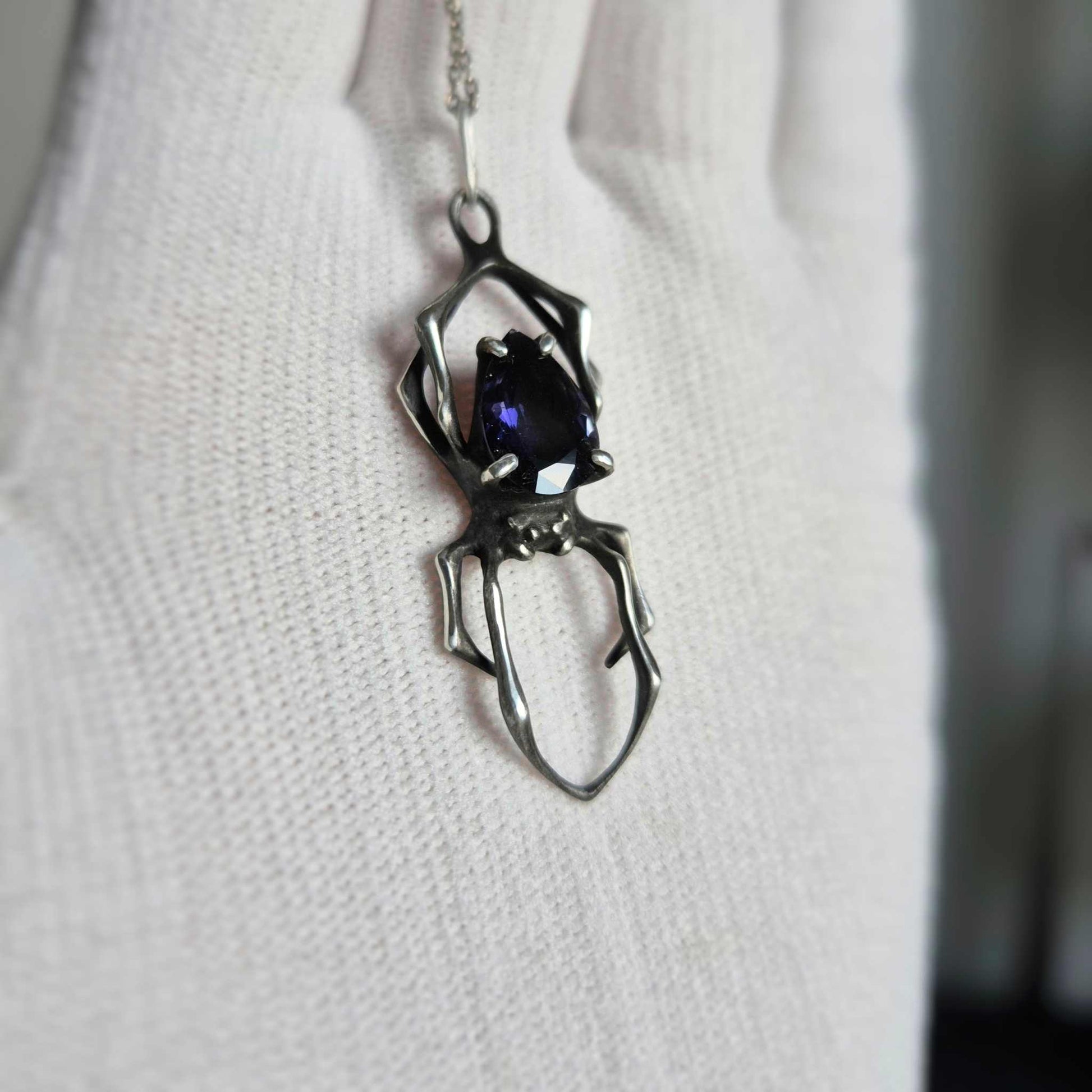 silver Spider necklace with faceted iolite sunstone shown on a white glove
