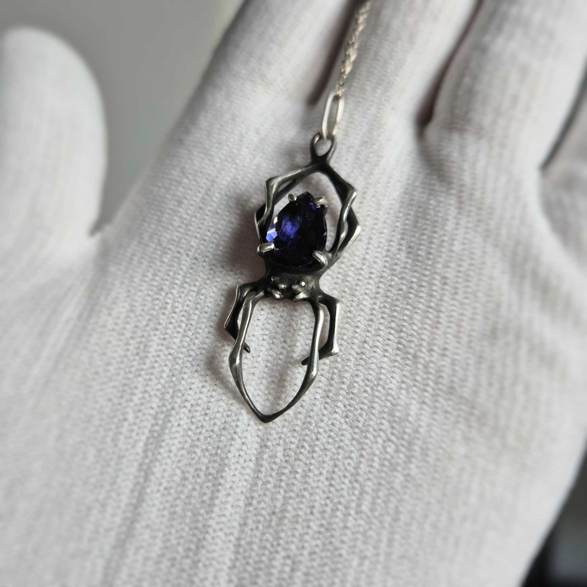 Elegant silver Spider necklace featuring iolite sunstone, gently displayed in a white-gloved hand