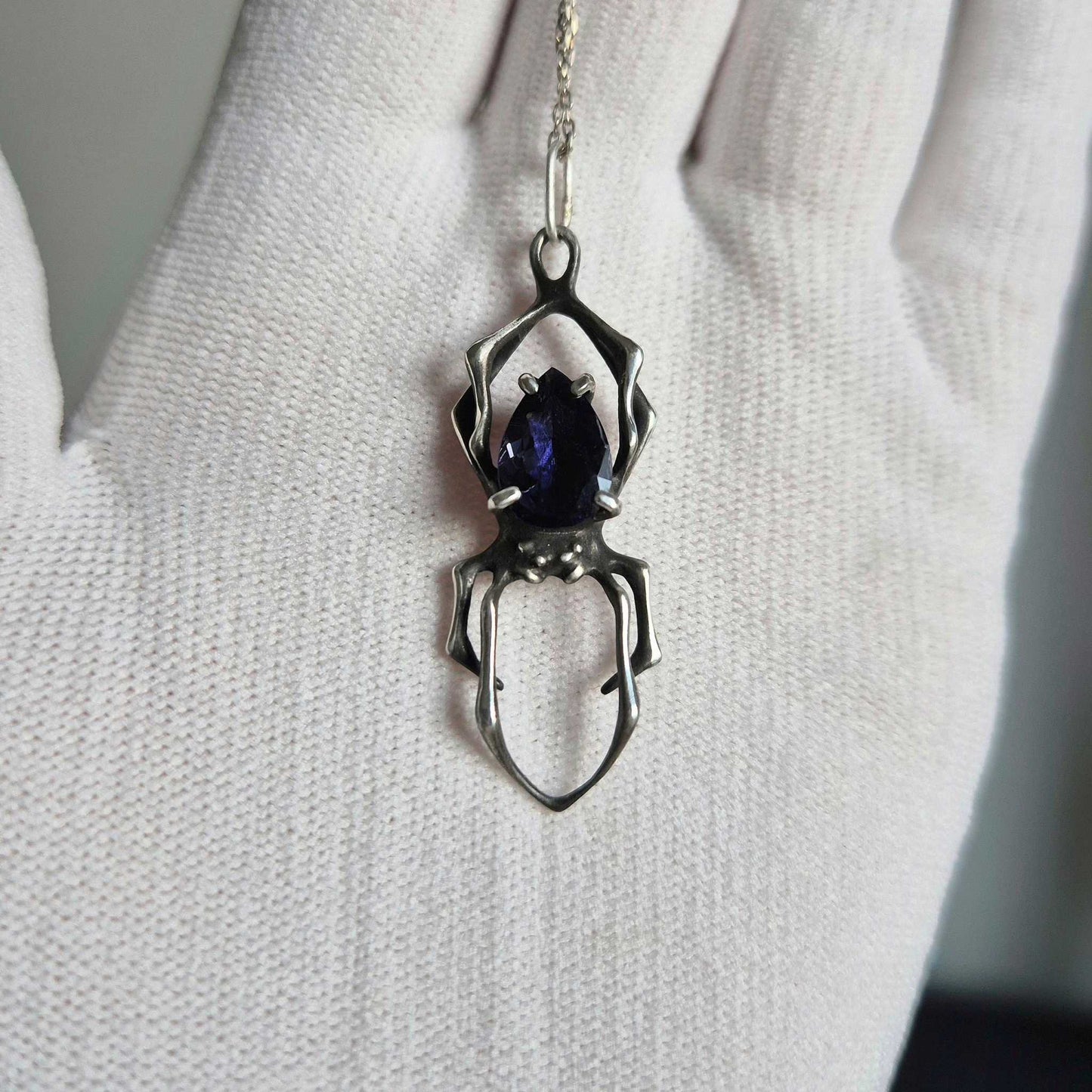 Handmade silver Spider pendant with shimmering iolite sunstone, shown on a white-gloved hand