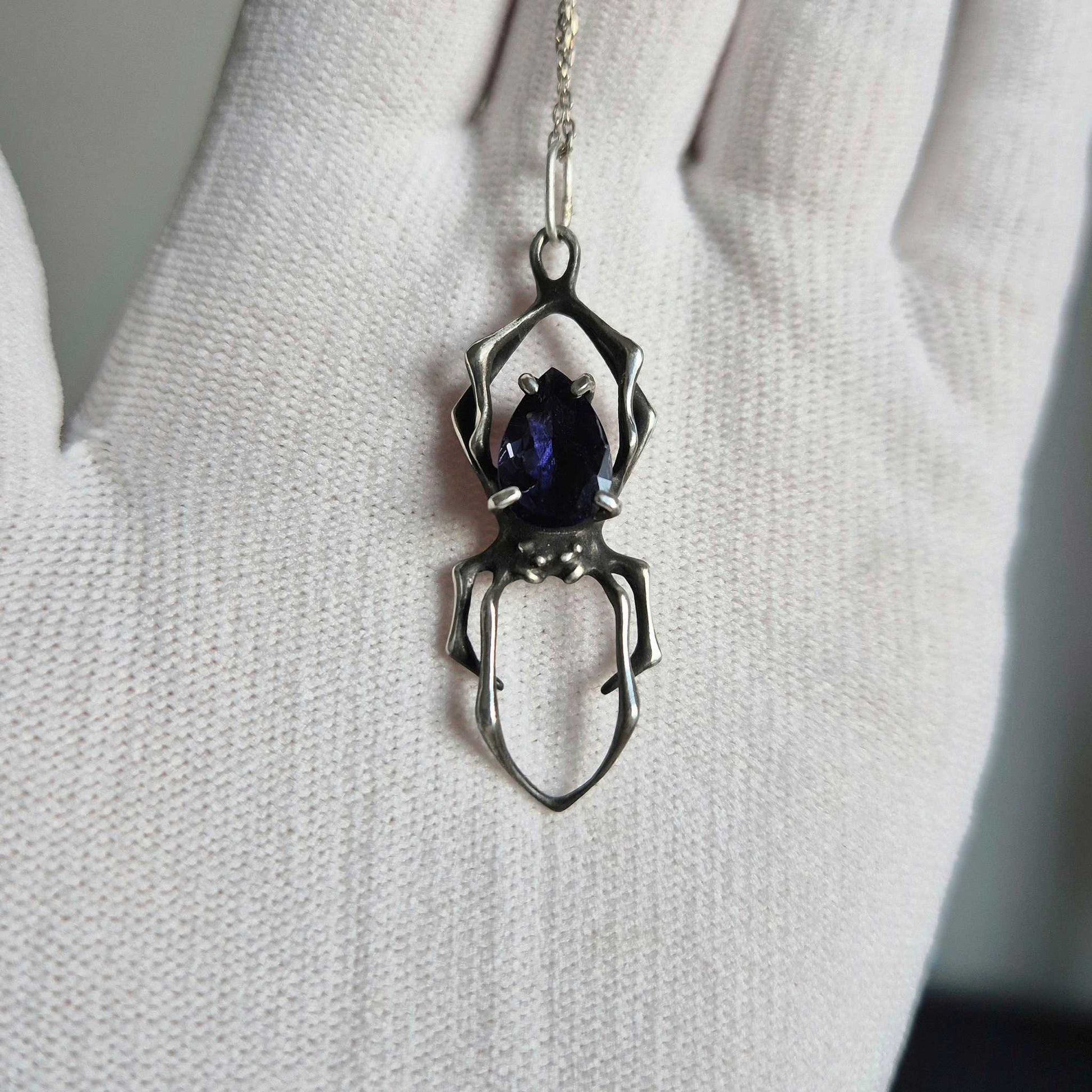 Handmade silver Spider pendant with shimmering iolite sunstone, shown on a white-gloved hand