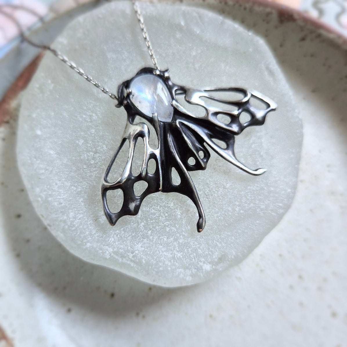 Detailed view of oxidized silver moth necklace with glowing rainbow moonstone