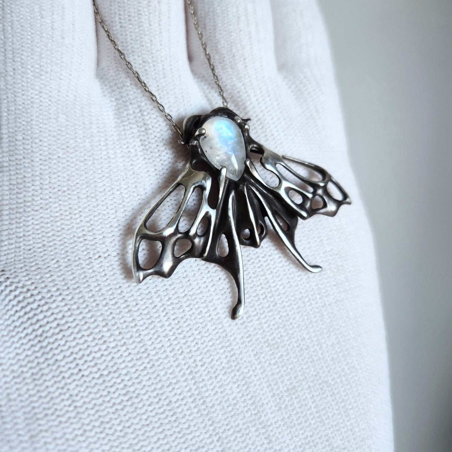 Handmade silver moth necklace with luminous moonstone, held in gloved hand