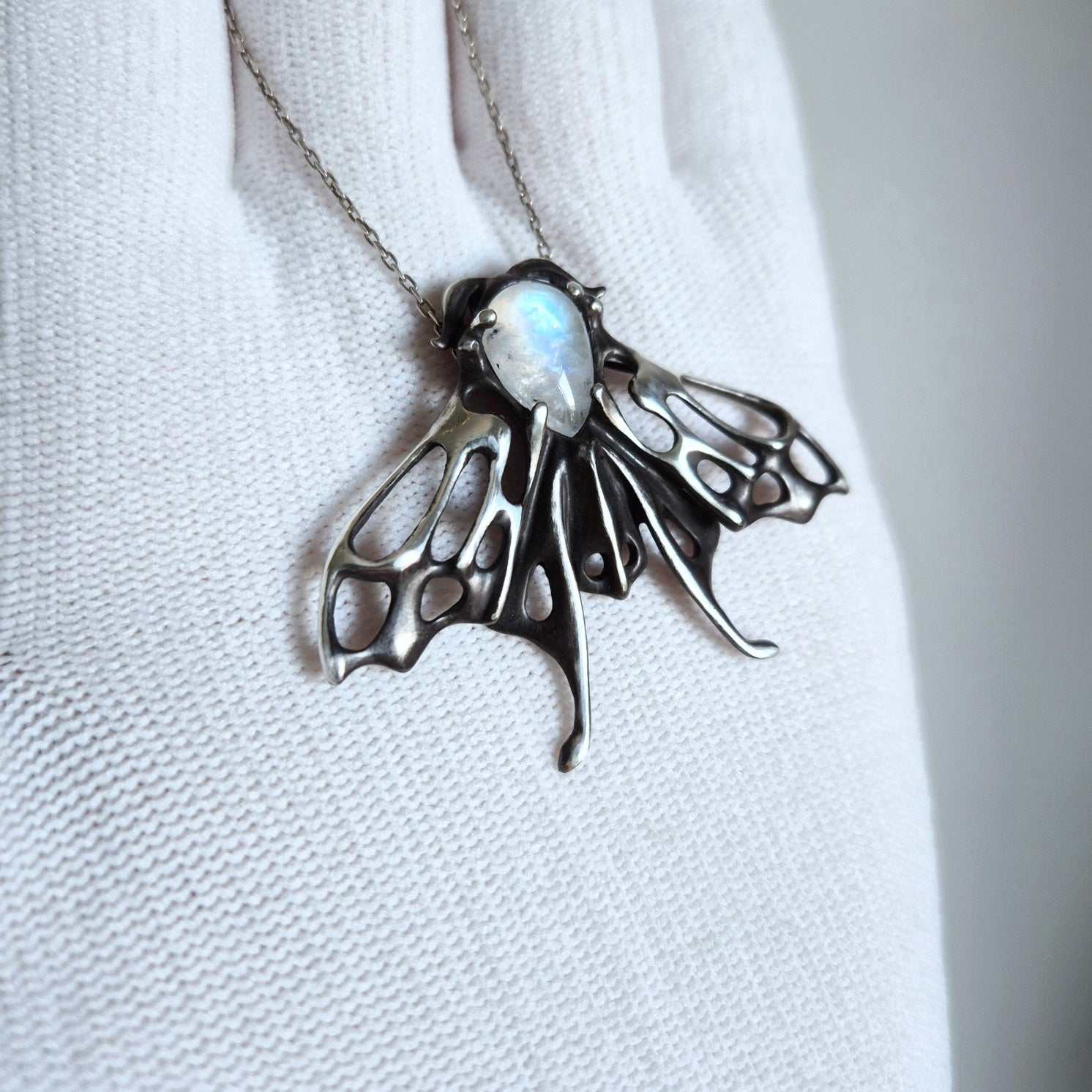 Handmade silver moth necklace with luminous moonstone, held in gloved hand