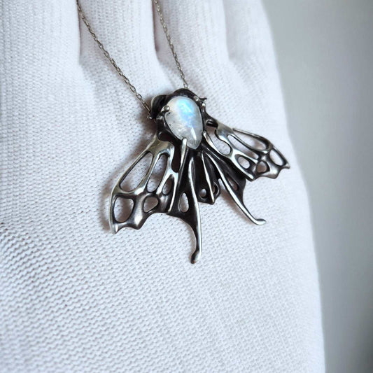 Handmade silver moth necklace with luminous moonstone, held in gloved hand