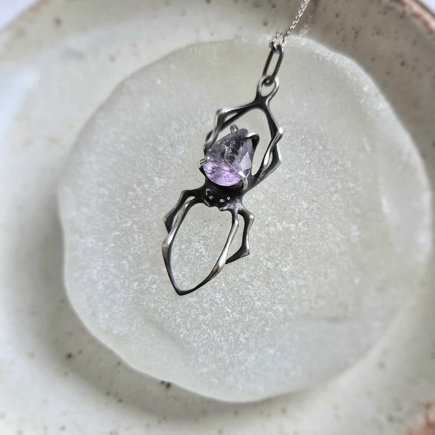 Detailed view of the silver Spider necklace with Super Seven gemstone from above, with light catching on the gem’s facets and inclusions.