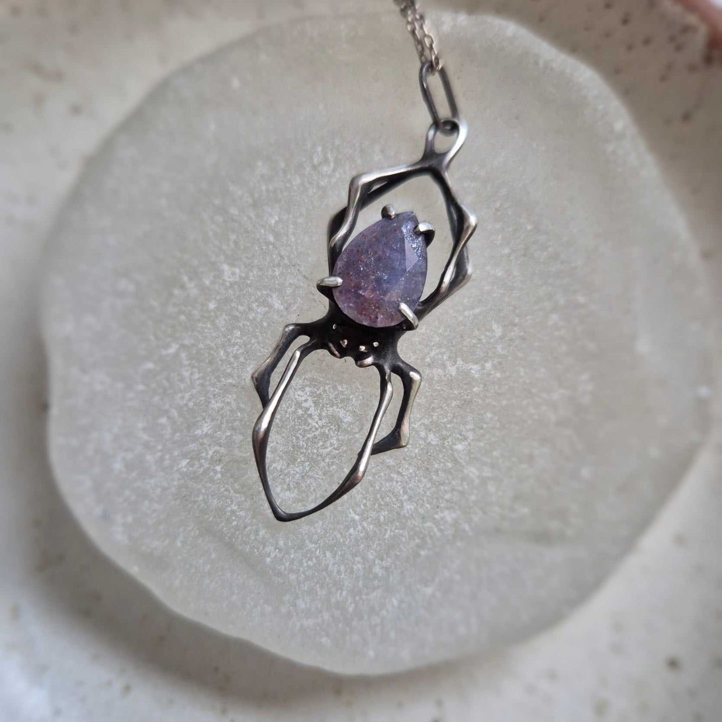 Silver Spider necklace with iolite sunstone cabochon, displayed on ceramic surface