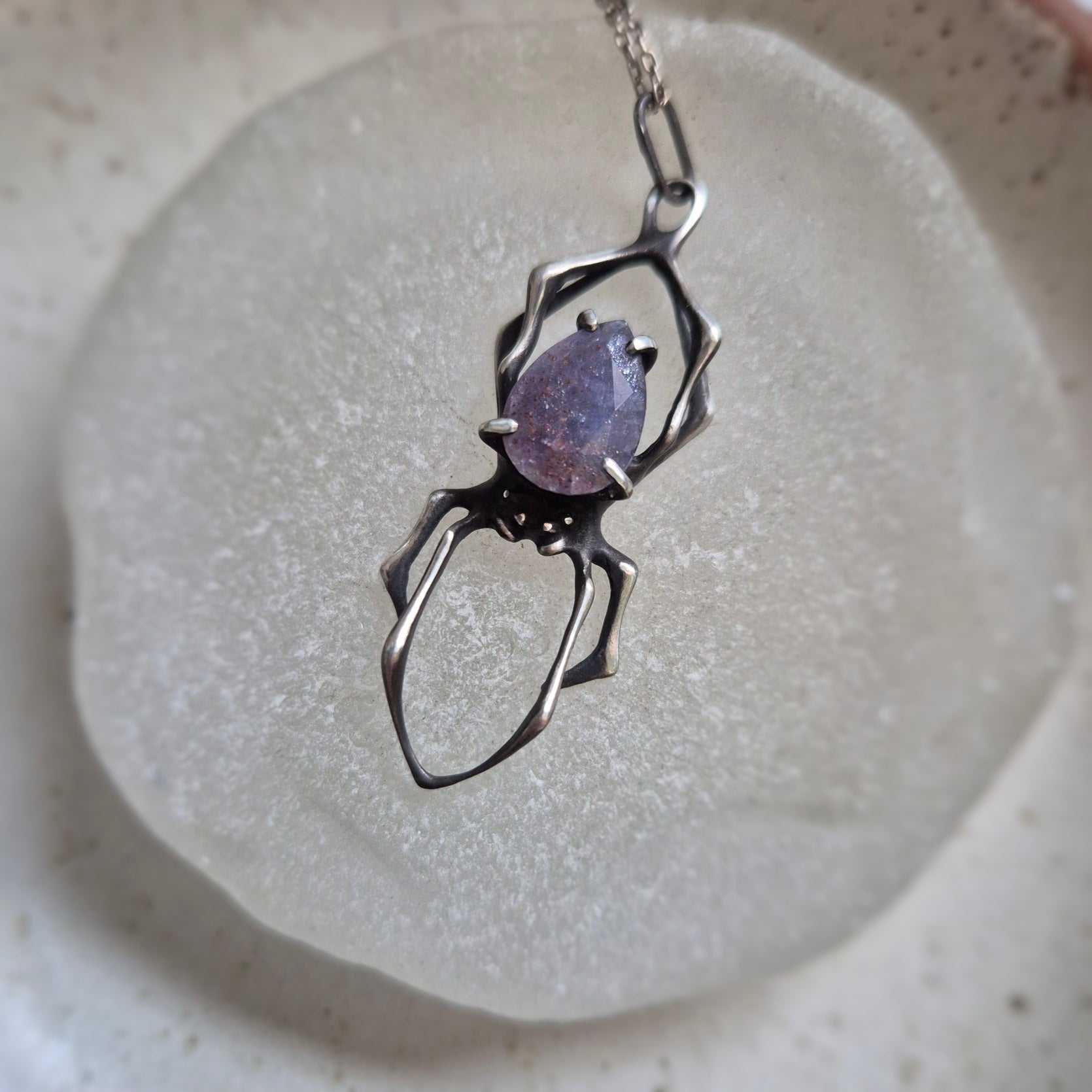 Silver Spider necklace with iolite sunstone cabochon, displayed on ceramic surface