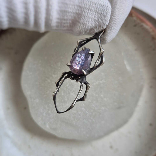 Silver Spider necklace with faceted iolite sunstone gemstone on round ceramic dish