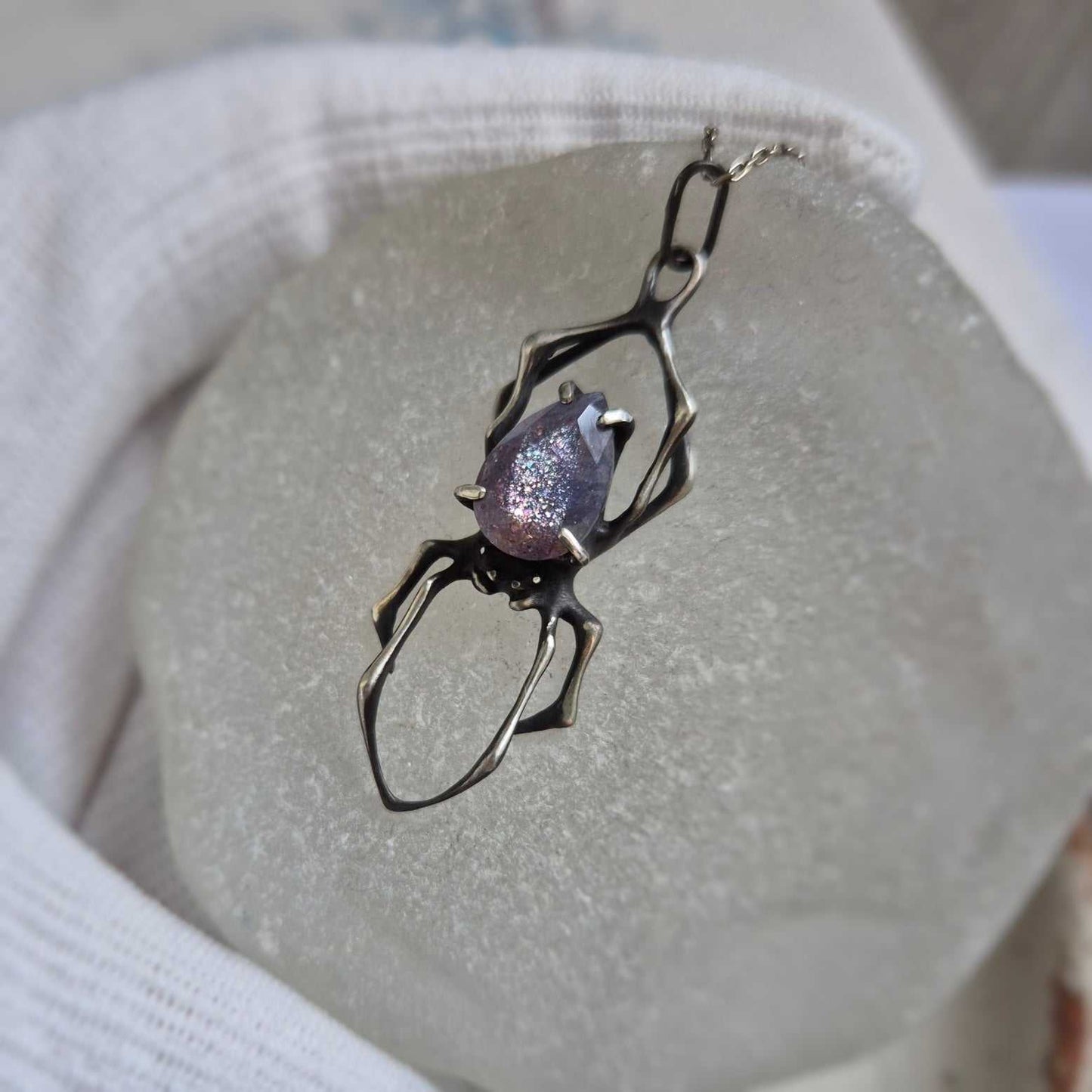 Handmade silver Spider pendant featuring iolite sunstone, photographed on pale backdrop