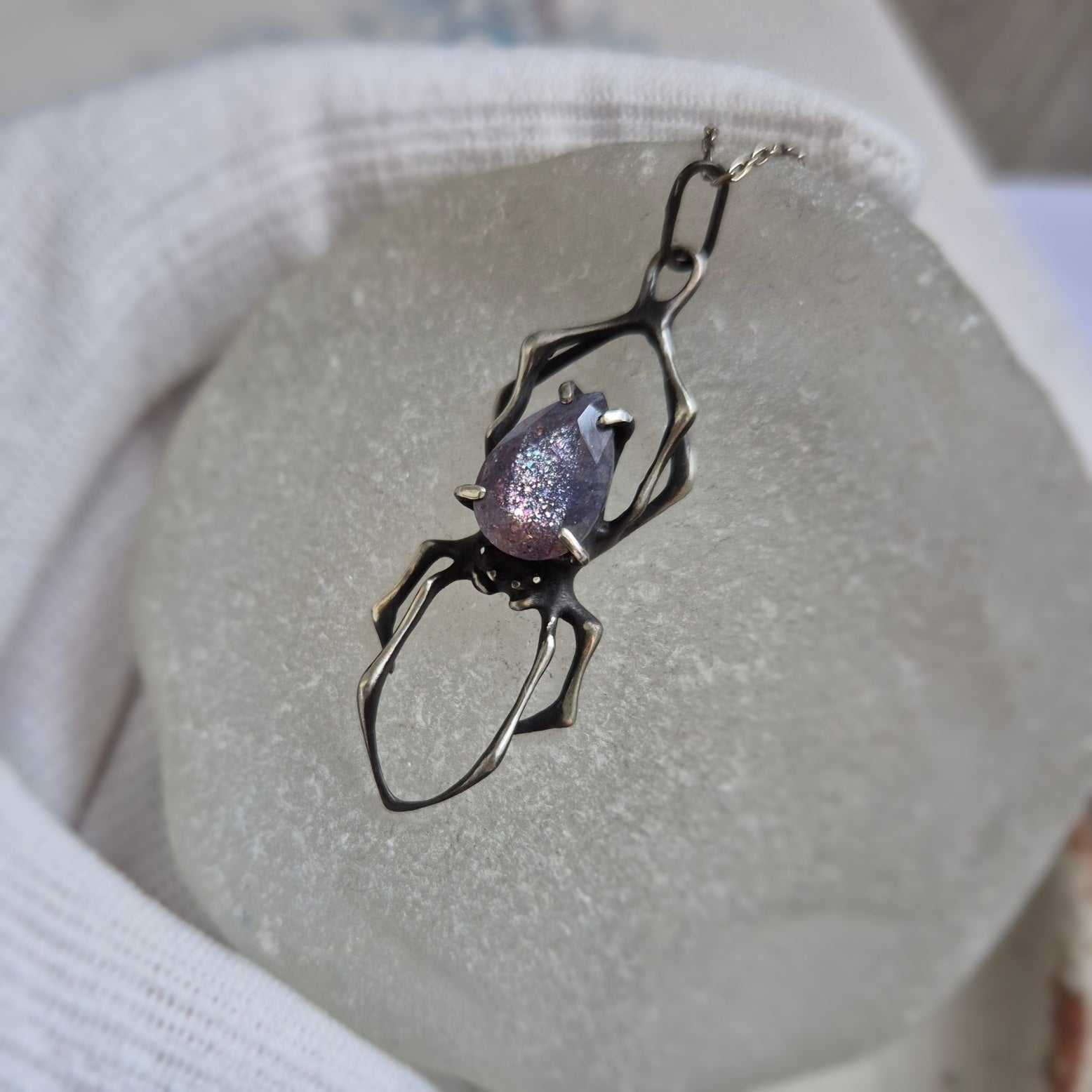 Handmade silver Spider pendant featuring iolite sunstone, photographed on pale backdrop