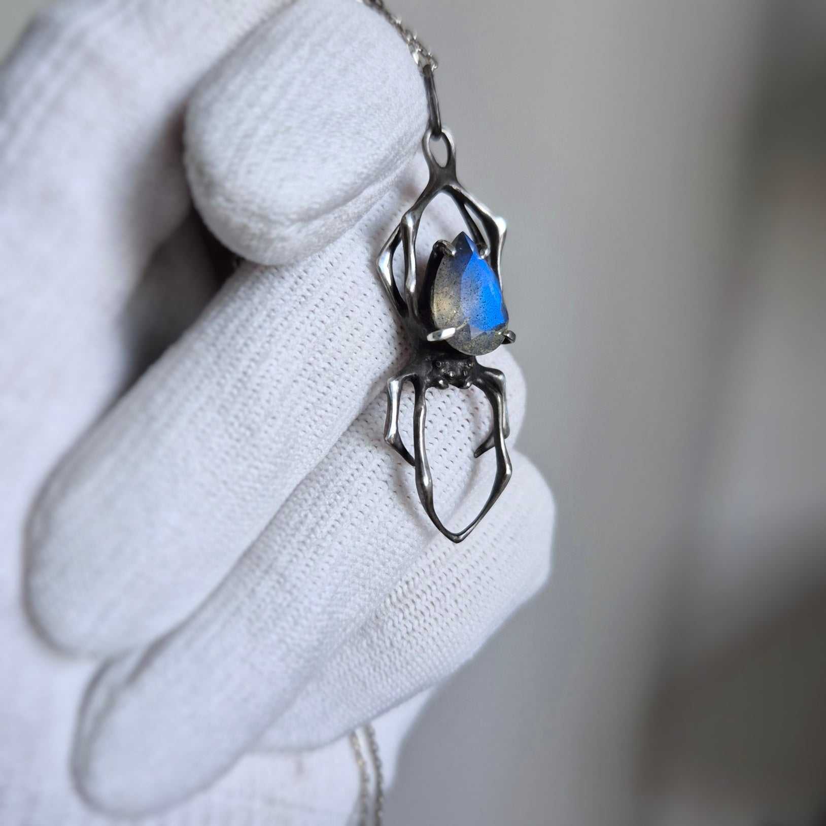 Sterling silver spider pendant with speckled blue gemstone in soft lighting