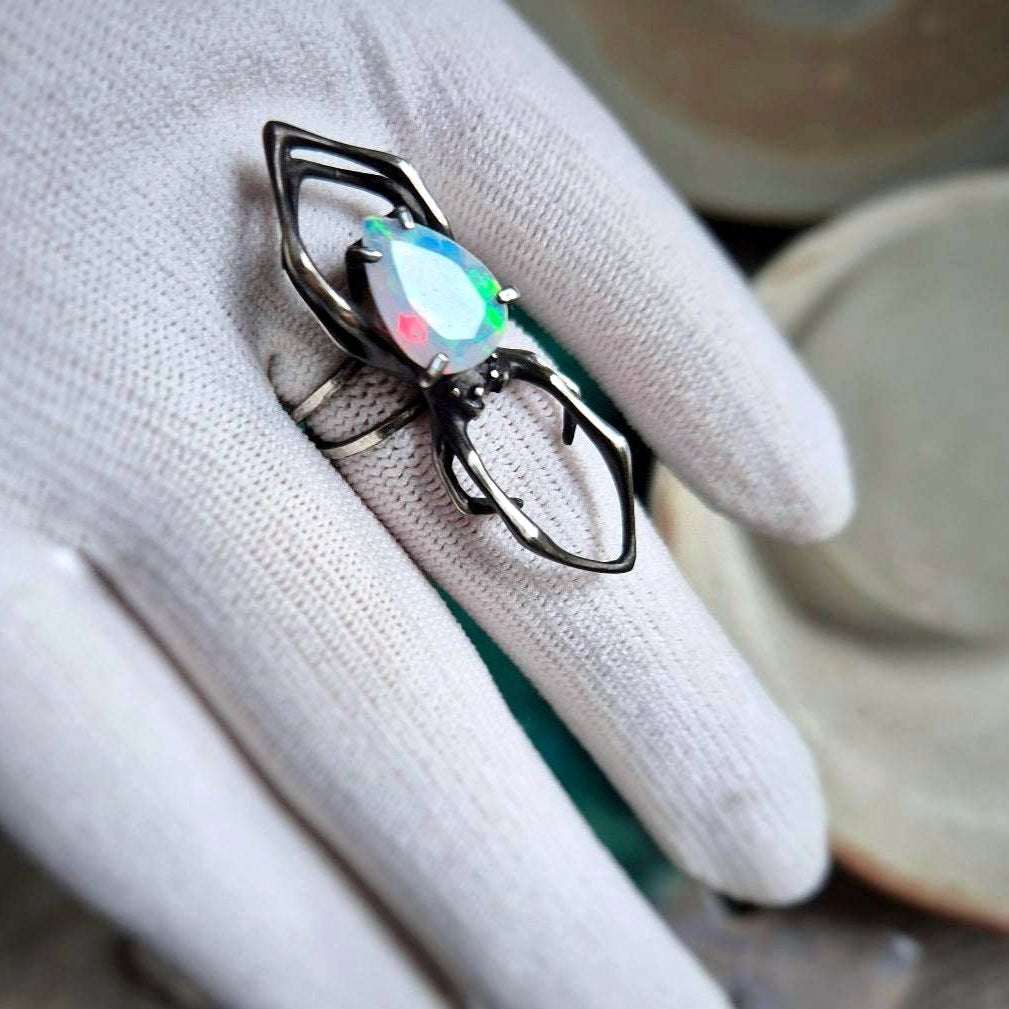 Handmade silver spider ring with glowing opal gemstone, angled on glove