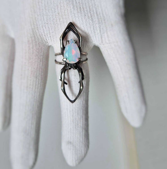 Silver spider ring with natural opal shown on a white glove, top view