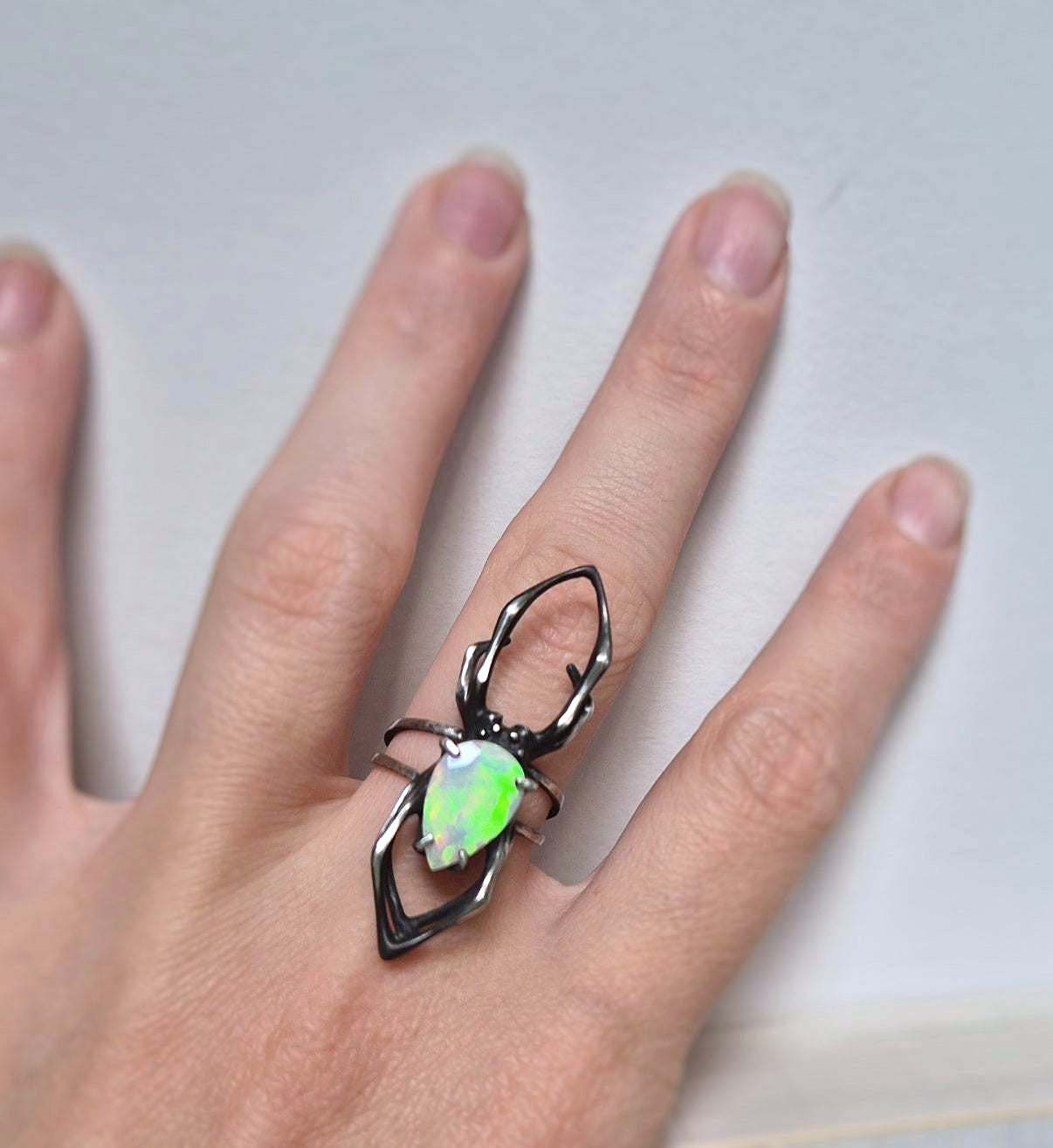 Silver spider ring with opal worn on hand, shown in natural lightin